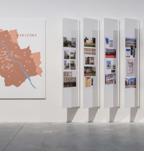 Zdjęcie przedstawiające mapę Warszawy i wertykalne panele przyczepione do ściany ze zdjęciami szkoł „tysiąclatek\