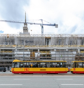 [kolorowe zdjęcie przedstawia budowę muzeum sztuki nowoczesnej w Warszawie na placu Defilad z perspektywy ul. Marszałkowskiej. Widać już dwie nadziemne kondygnacje budynku. Całość przesłonięta jest rusztowanie i siatką budowlaną, pod któr powstaje jednolit