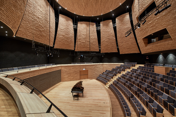 Sala koncertowa z fortepianem na scenie, puste siedziska i drewniane panele akustyczne.