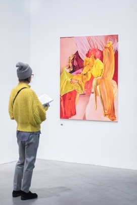[photo of a parson in a yellow jacket watching a painting with a couple of yellow colours combined with orange and red]