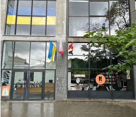 Zdjęcie. Budynek Muzeum przy ulicy Pańskiej 3. W oknach budynku odbija się deszczowe niebo. Na ścianach powiewają flagi Ukrainy.
