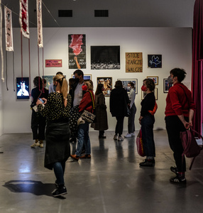 Kolorowe zdjęcie przedstawiające widzów wystawy patrzących na sztandary, banery z protestów i fotografie, za nimi bordowa kotara – element scenografii wystawy.