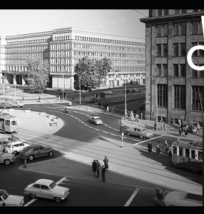 Czarno-białe, archiwalne zdjęcie powojennej Warszawy pokazuje rondo do Gaulle\'a. Przez środek przejeżdża tramwaj, a na około jeżdżą samochody. Po pasach przechodzi niewielka grupa pieszych. W prawym, górnym rogu jest logo festiwalu Warszawa w Budowie.