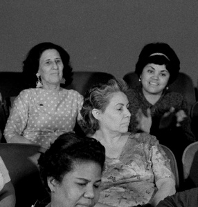 Zdjęcie. Carno-białe. Grupa ośmiu kobiet, widziana od przodu, siedzi w fotelach kinowych i rozmawia ze sobą.
