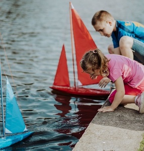 Zdjęcie. Dzieci puszczają kolorowe modele łódek po stawie w parku/