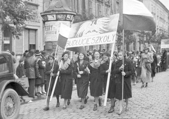 Zdjęcie czarno-białe przedstawiające kobiety niosące transparent z napisem: budujcie szkoły.