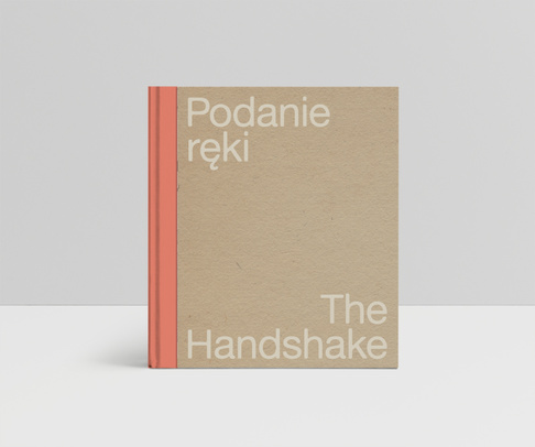 Beżowa okładka z pomarańczowym grzbietem i białym napisem: Podanie ręki i po angielsku: The Handshake