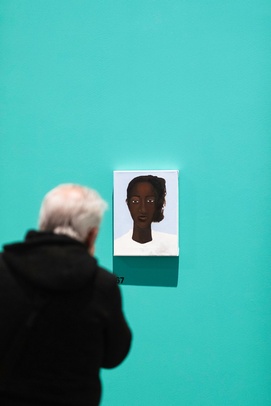 [na zdjęciu z wystawy osoba w czarnym płaszczu ogląda obraz zawieszony na zielonej ścianie]