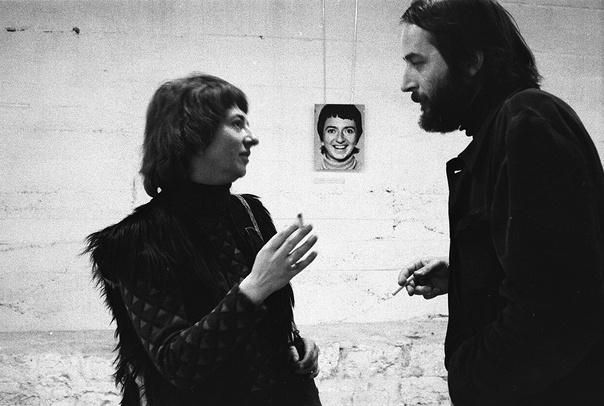 Zdjęcie czarno-białe. Anka Ptaszkowska stoi na przeciwko Niela Toroni. Oboje trzymają w ręku papierosy. Rozmawiają. W tle na murowanej ścianie widać zawieszone zdjęcie uśmiechniętej Ptaszkowskiej.