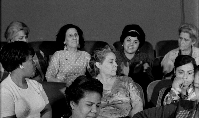 Zdjęcie. Carno-białe. Grupa ośmiu kobiet, widziana od przodu, siedzi w fotelach kinowych i rozmawia ze sobą.