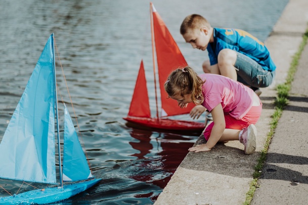 Zdjęcie. Dzieci puszczają kolorowe modele łódek po stawie w parku/
